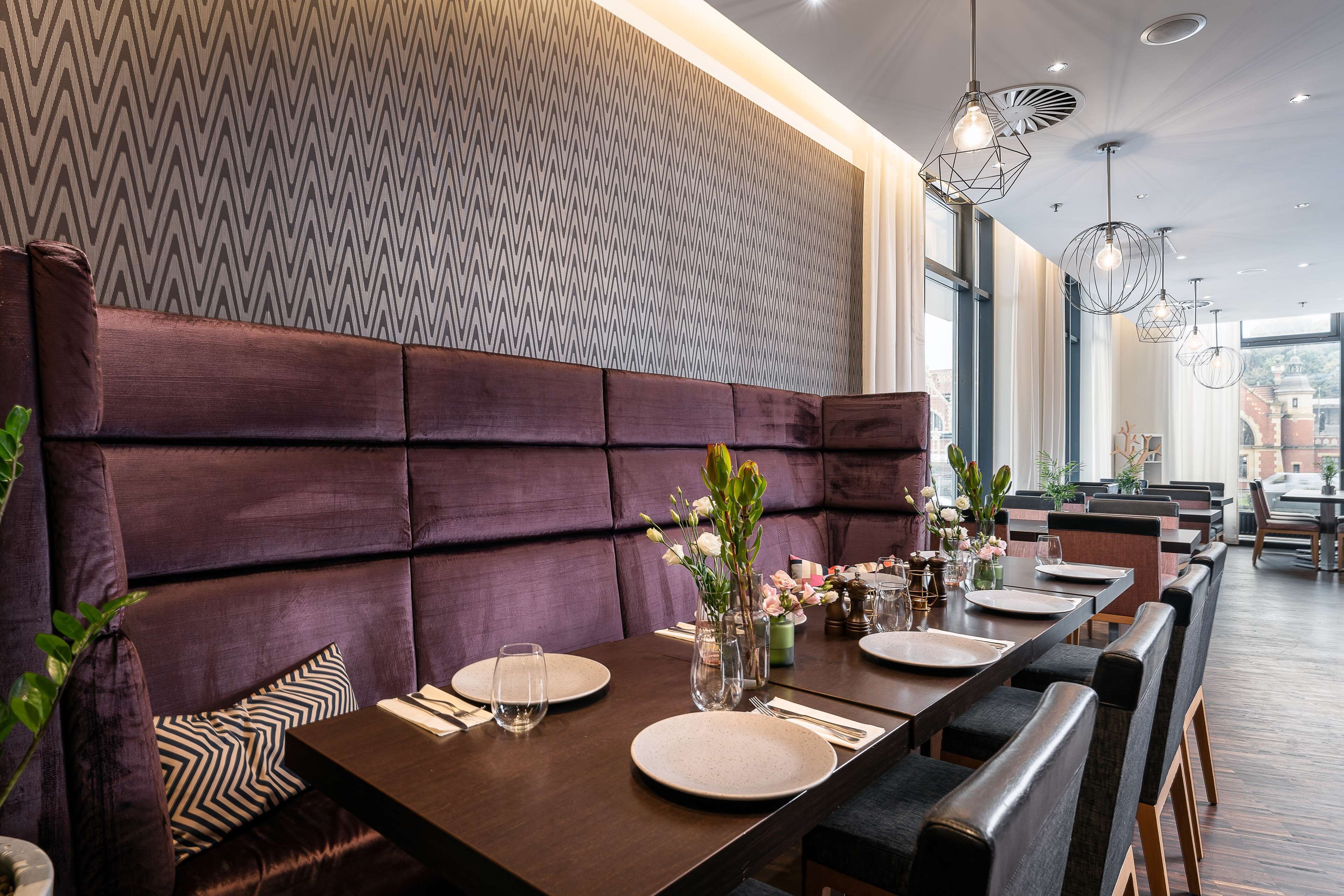 A dining area with a long table set for four, cushioned seating, and pendant lighting.