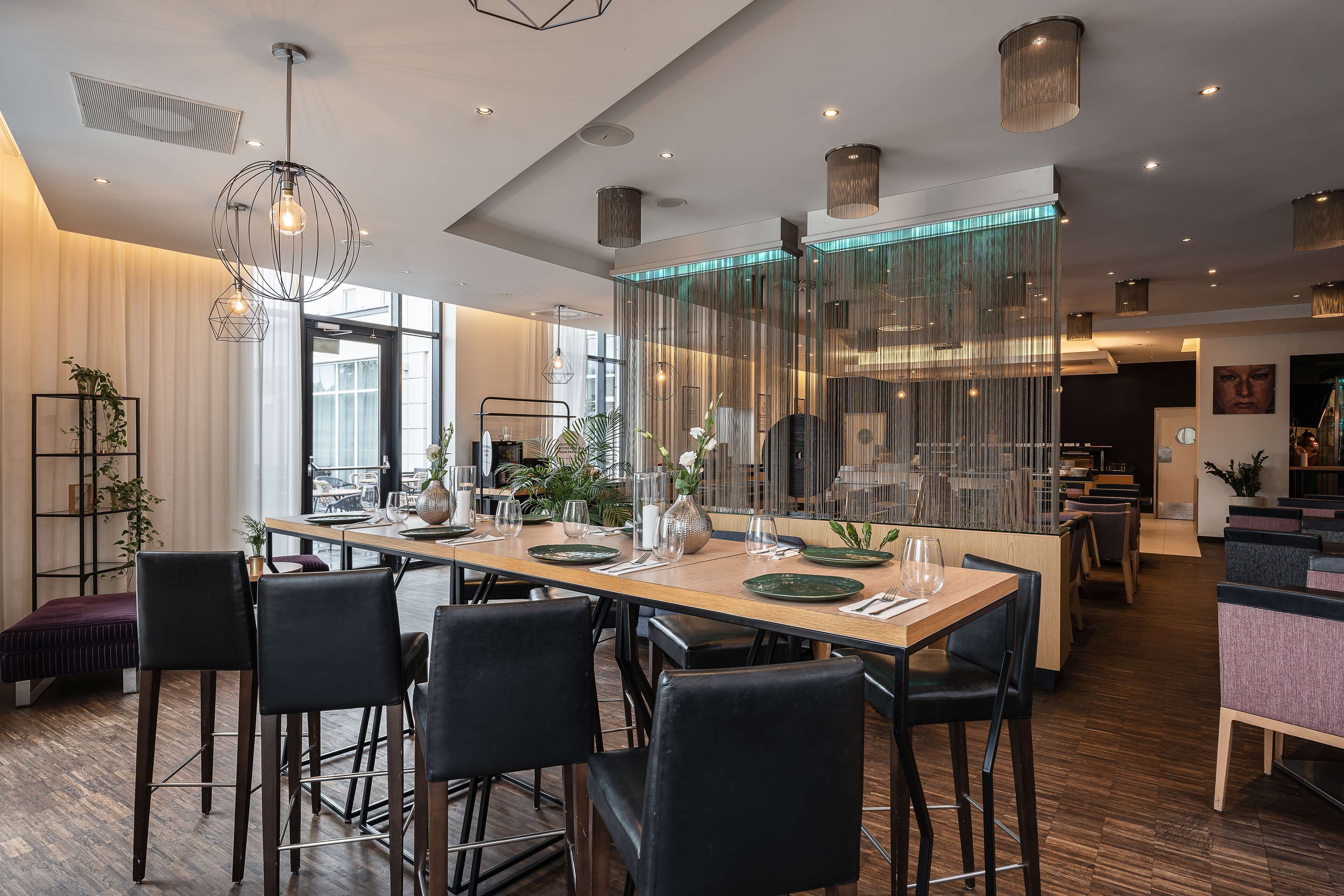A modern dining area with a long table set for six, surrounded by black chairs.