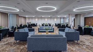 Una sala de conferencias moderna con mesas redondas, sofás grises y suelo alfombrado.