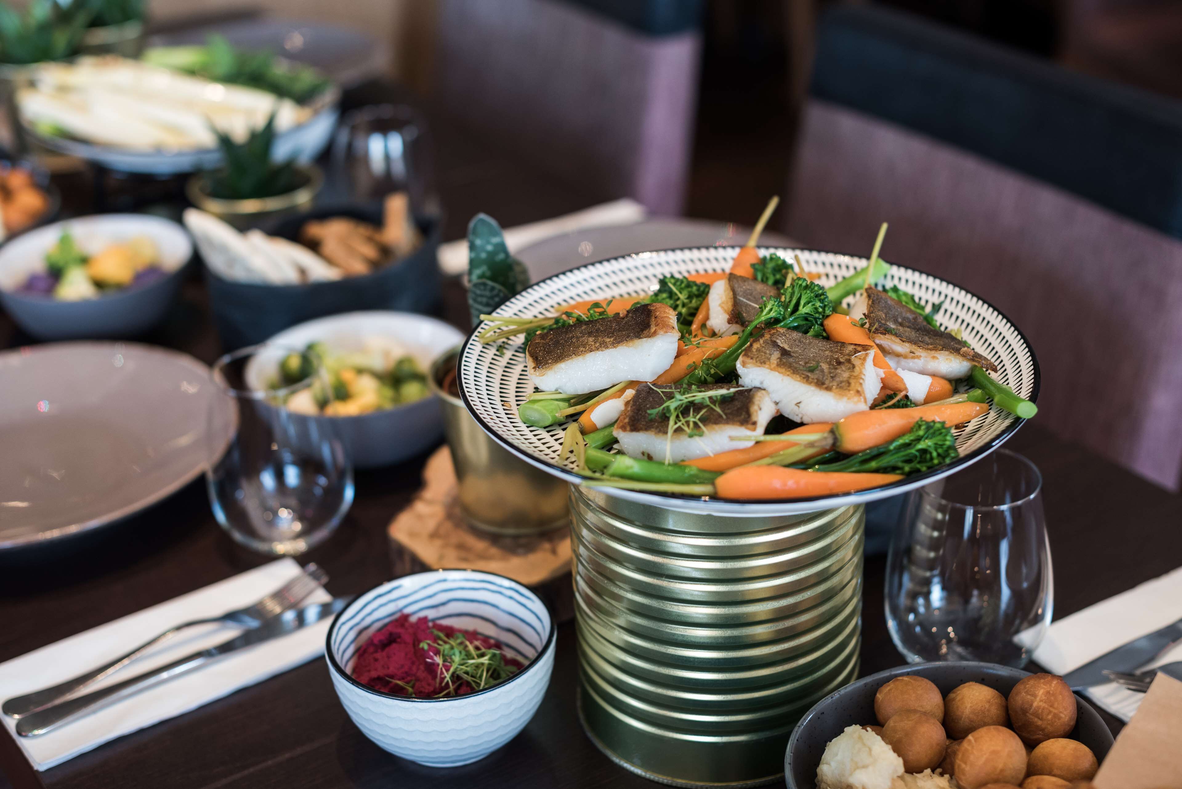 Ein Esstisch mit verschiedenen Speisen, darunter ein Fischgericht mit Gemüse, umgeben von Salatschüsseln und anderen Lebensmitteln.