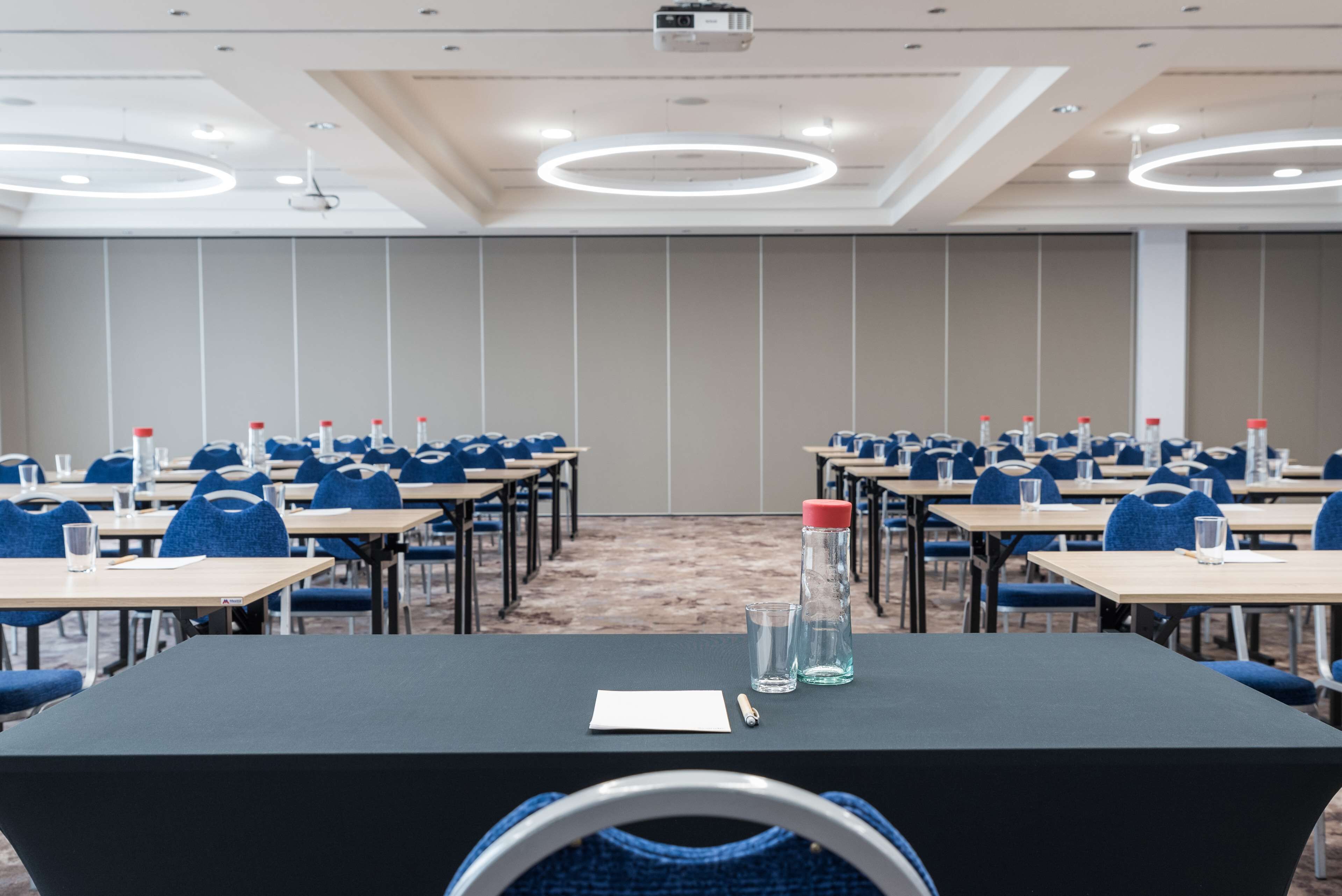 A conference room with rows of tables and chairs, equipped with water bottles and glasses.