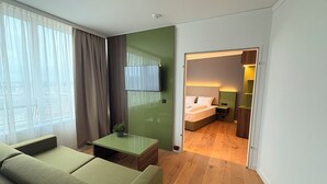 Una habitación de hotel moderna con una pared verde decorativa, un televisor de pantalla plana, una cama con cabecera, una mesita de noche y una planta pequeña.