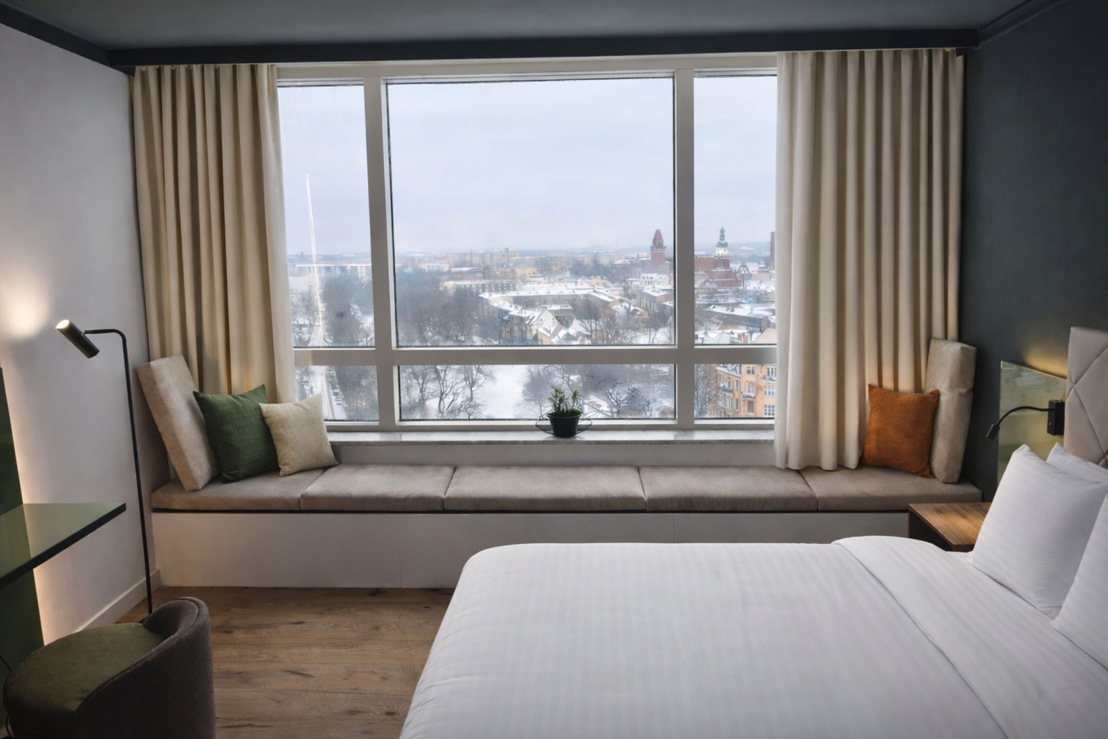 A hotel room with a large window, a bed, a bedside table, and a chair.