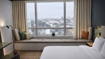 A hotel room with a large window, a bed, a bedside table, and a chair.