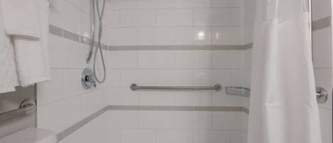 A bathroom with white tiles, a shower with a handheld showerhead, a grab bar, and a towel rack.