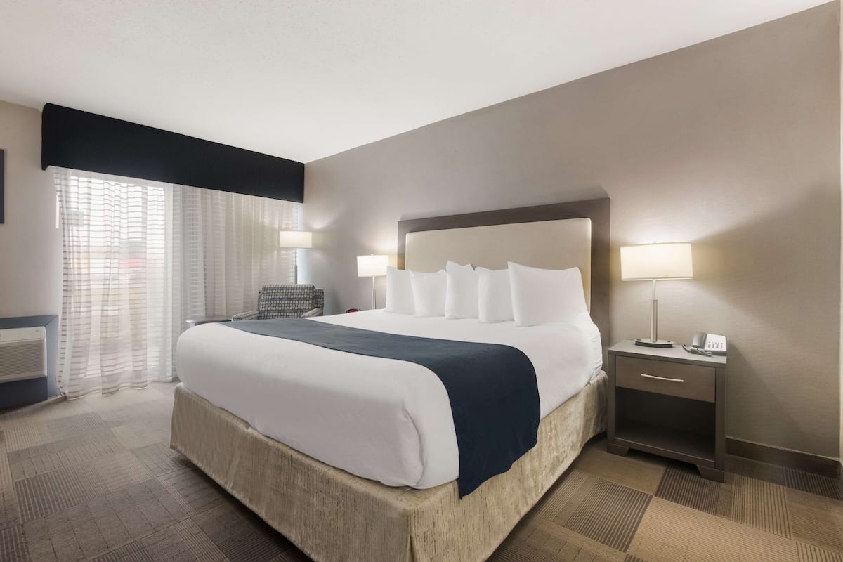 A hotel room with a large bed, bedside tables with lamps, a chair, and a window with curtains.