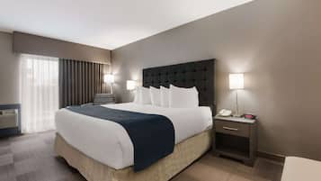 A hotel room with a large bed, a bedside table with a lamp, and a window with curtains.