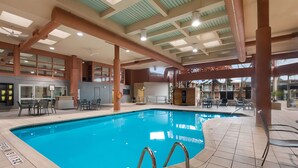Une piscine intérieure à l’eau claire, entourée d’un sol carrelé et de rampes en métal.