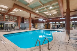 Una piscina interior con agua cristalina, rodeada de suelo de baldosas y barandillas de metal.
