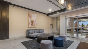 Un hall d’entrée moderne avec un canapé gris, une table basse en bois et deux poufs.