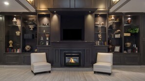 Una sala de estar moderna con chimenea, dos sillones y estanterías empotradas con objetos decorativos.