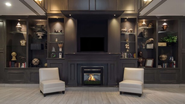 Un salon moderne doté d’une cheminée, de deux fauteuils et d’étagères intégrées où sont exposés des objets décoratifs.