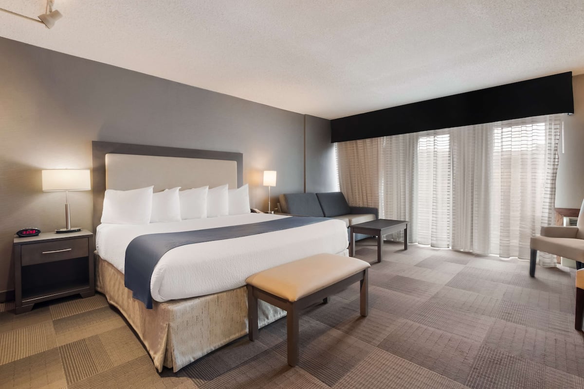 A hotel room with a large bed, bedside tables, a bench, a desk, and a chair.