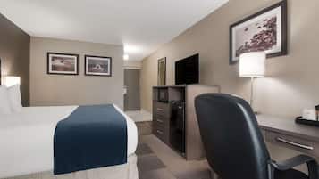 Habitación de hotel con cama, escritorio, silla, televisor, lámpara y dos cuadros en la pared.