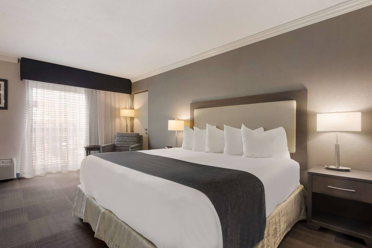 A hotel room with a large bed, two bedside tables with lamps, a chair, and a window with curtains.