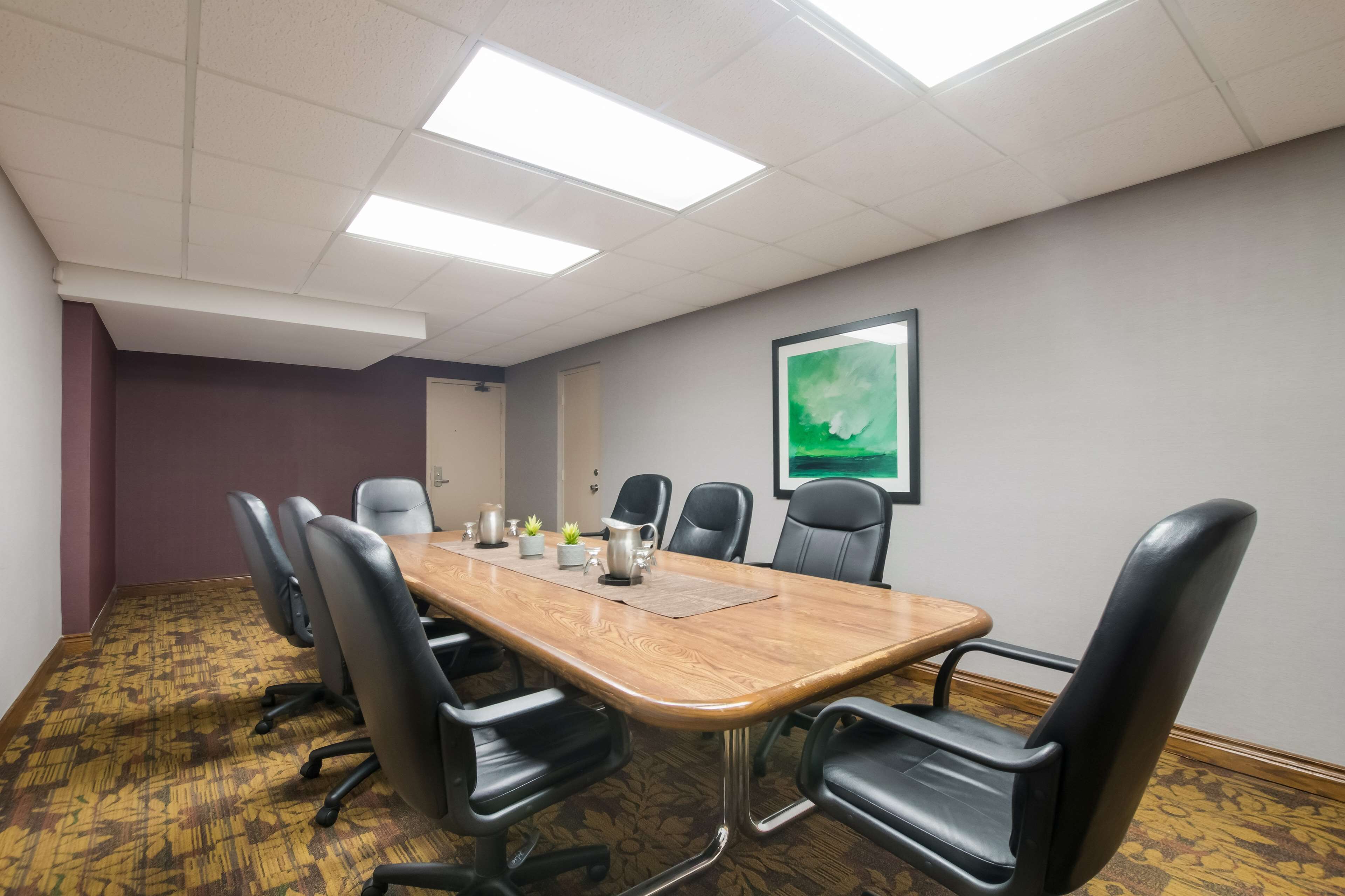 A conference room with a long wooden table, black chairs, and a green abstract painting on the wall.