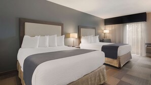 Une chambre d’hôtel avec deux lits, une grande fenêtre avec des rideaux et un téléviseur à écran plat fixé au mur.