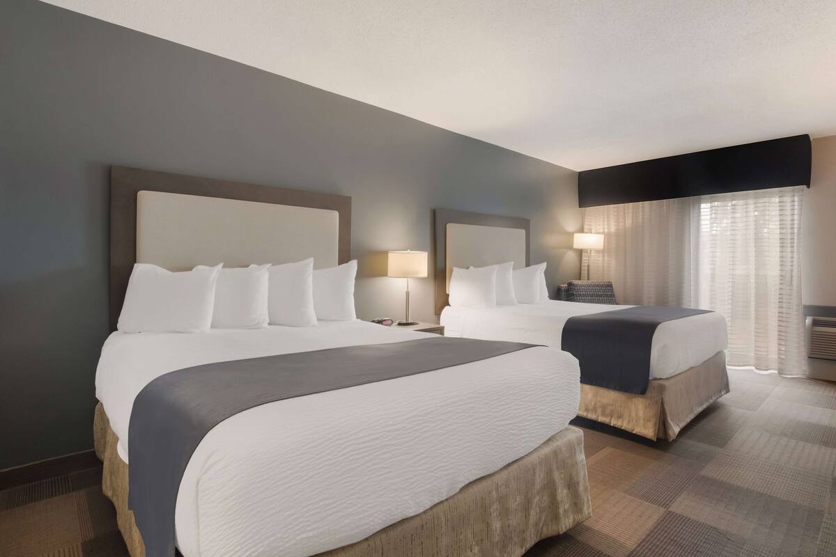 A hotel room with two beds, a large window with curtains, and a flat-screen TV mounted on the wall.