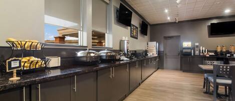 Una cocina moderna con armarios oscuros, encimera de granito y un comedor con mesa y sillas.