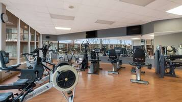 A gym with various exercise equipment, a large mirror, and a clock on the wall.