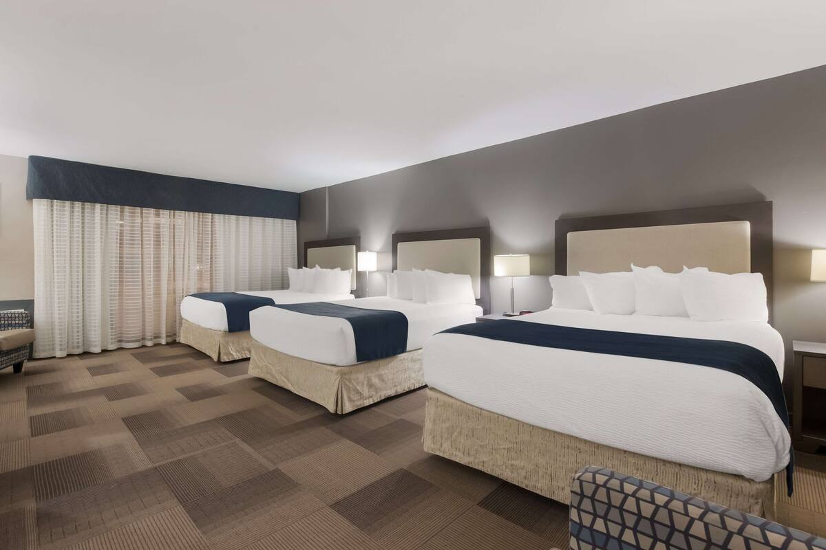 A hotel room with two beds, a desk, a chair, and a window with curtains.