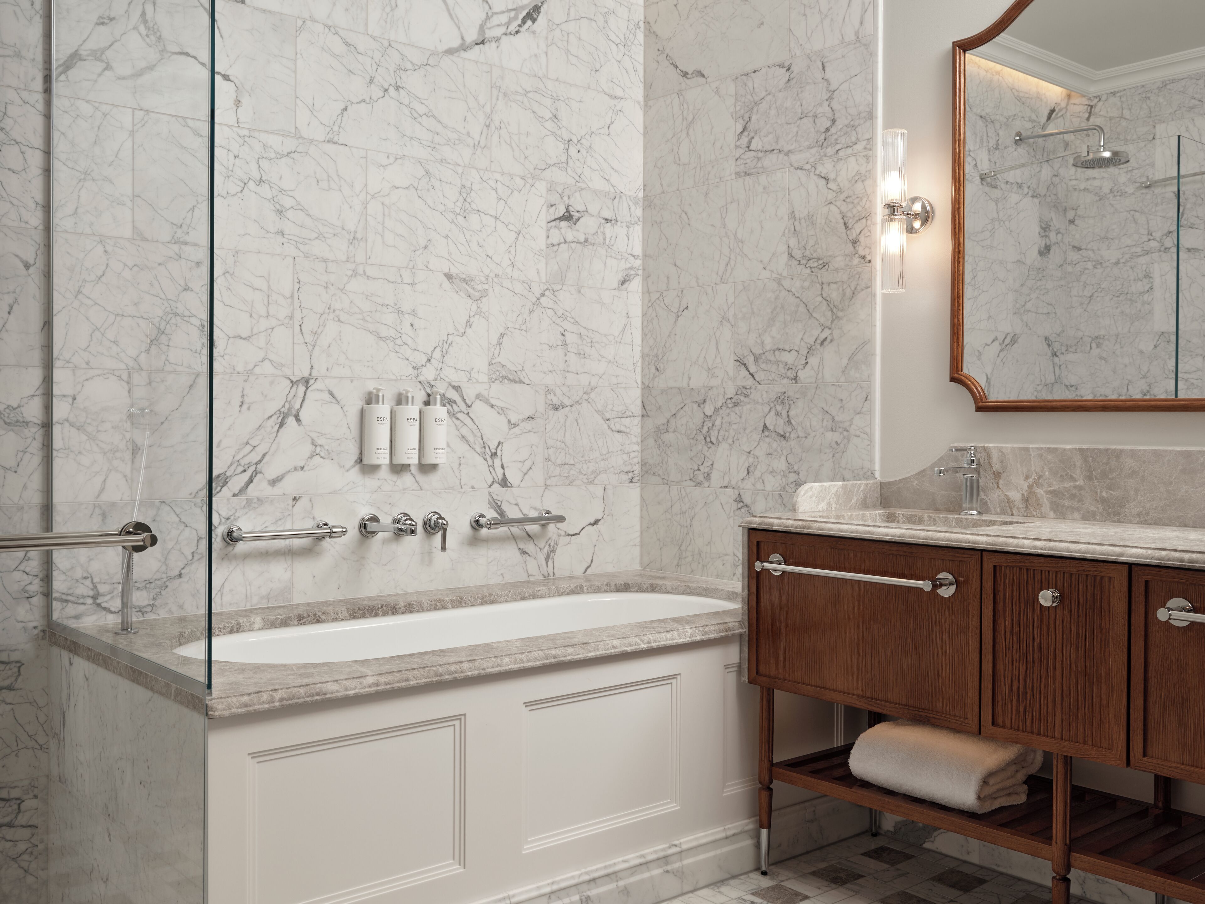 A bathroom with a marble wall, a bathtub, a wooden vanity, and a mirror.