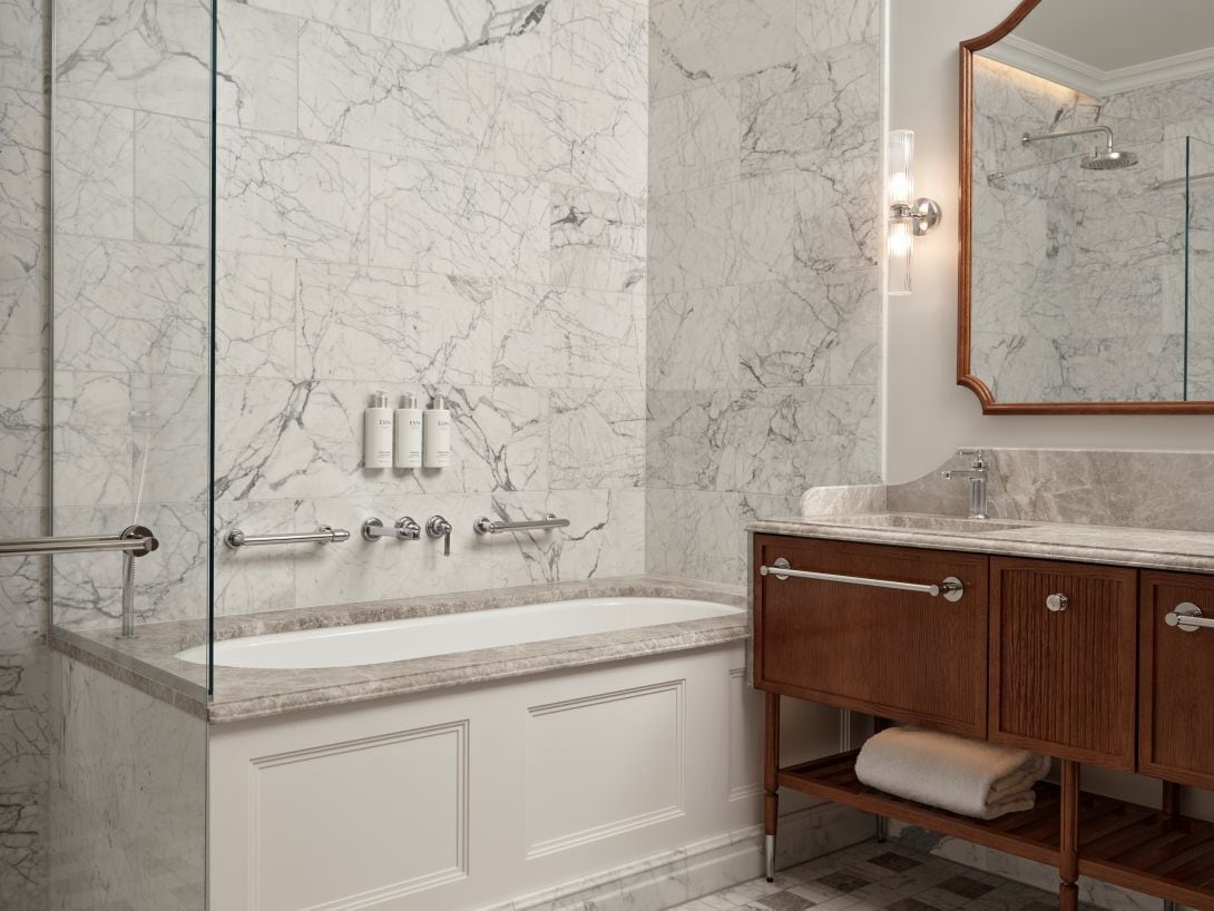 Un baño con pared de mármol, una bañera, un tocador con espejo y un perchero para toallas.