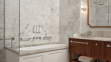 Un baño con pared de mármol, una bañera, un tocador con espejo y un perchero para toallas.