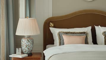 A neatly made bed with white linens, a wooden nightstand with a floral lamp, and a wall-mounted decorative piece.