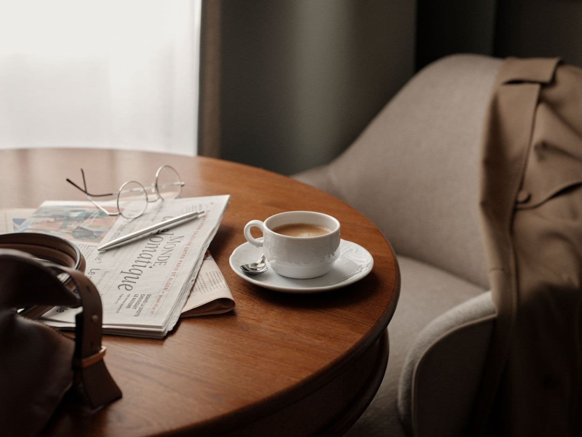 Una mesa de madera redonda con una taza de café, un par de gafas y un periódico.