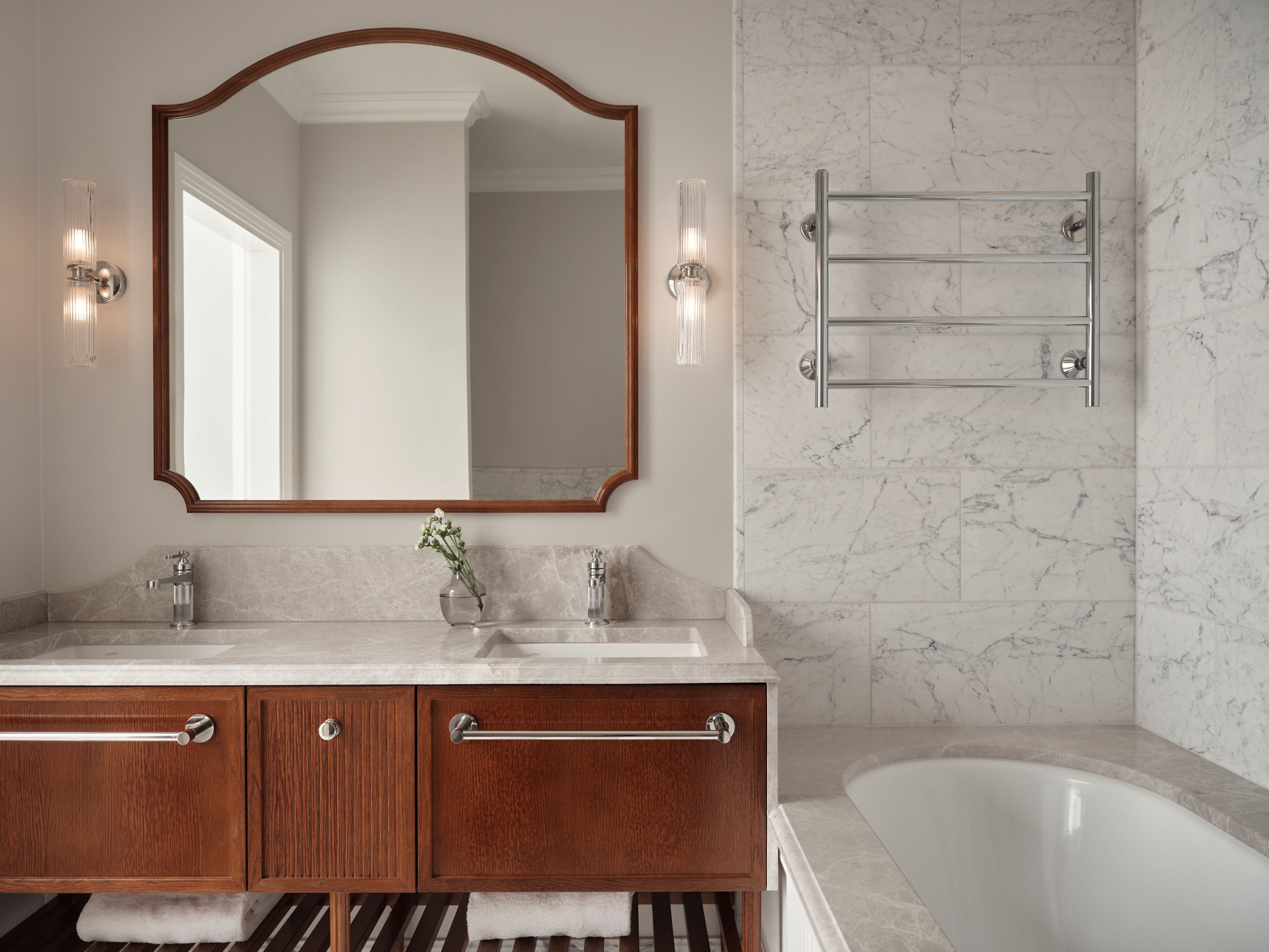 Un baño con tocador de madera, un espejo grande, toallero y bañera.