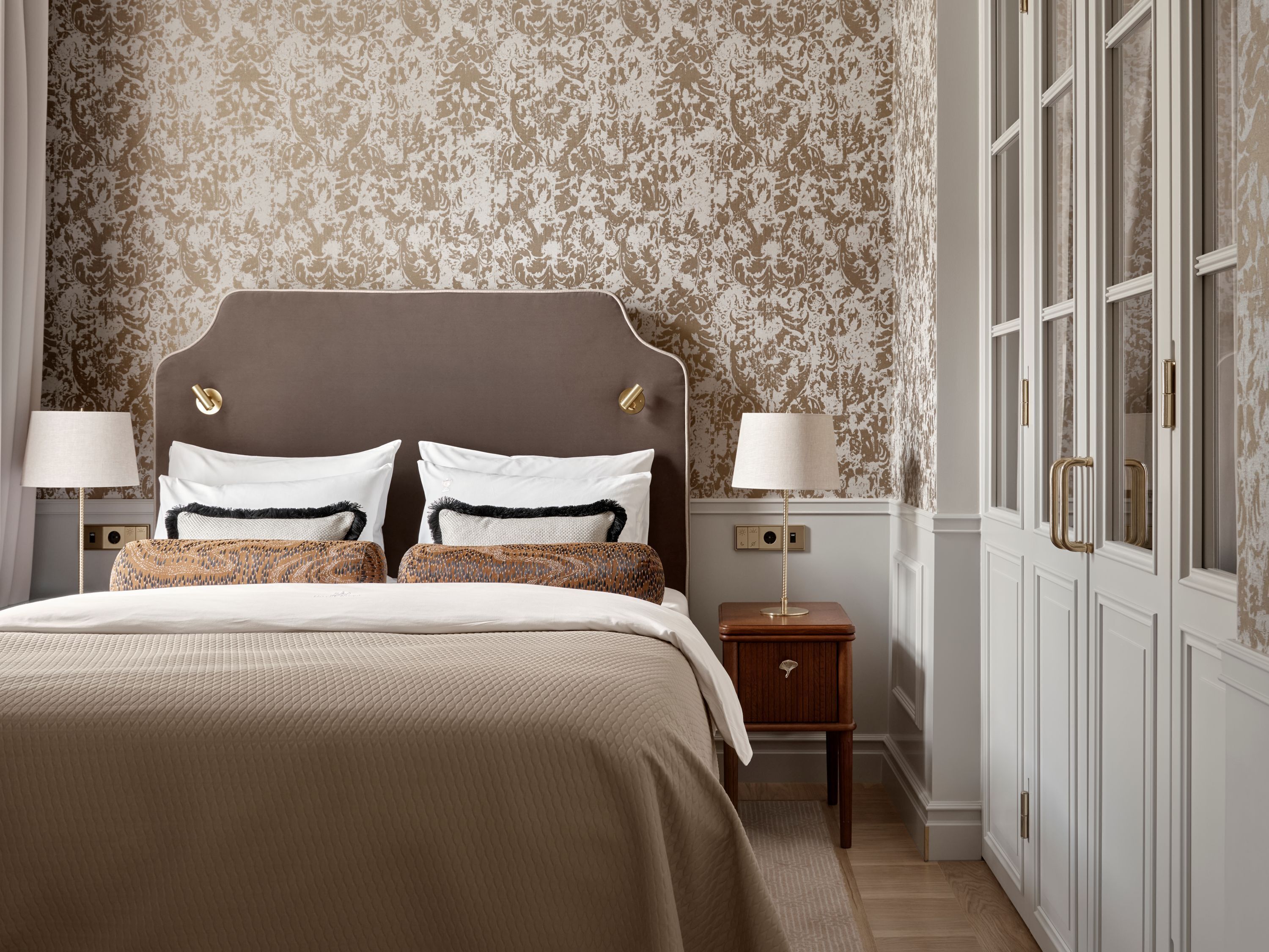 A bedroom with a large bed, two bedside tables, a nightstand, and a wardrobe.