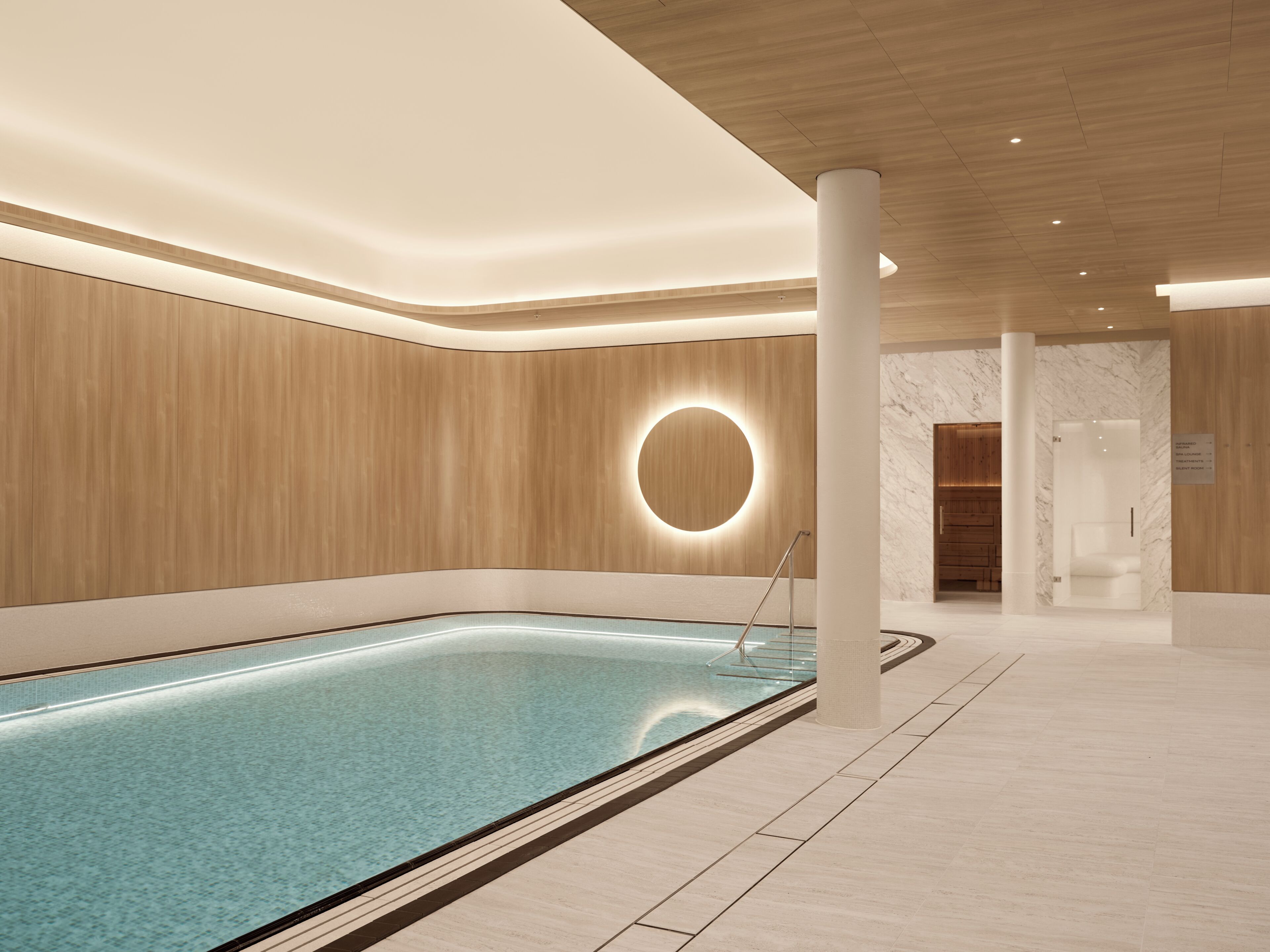 Une piscine intérieure moderne avec un mur en bois et un luminaire circulaire.