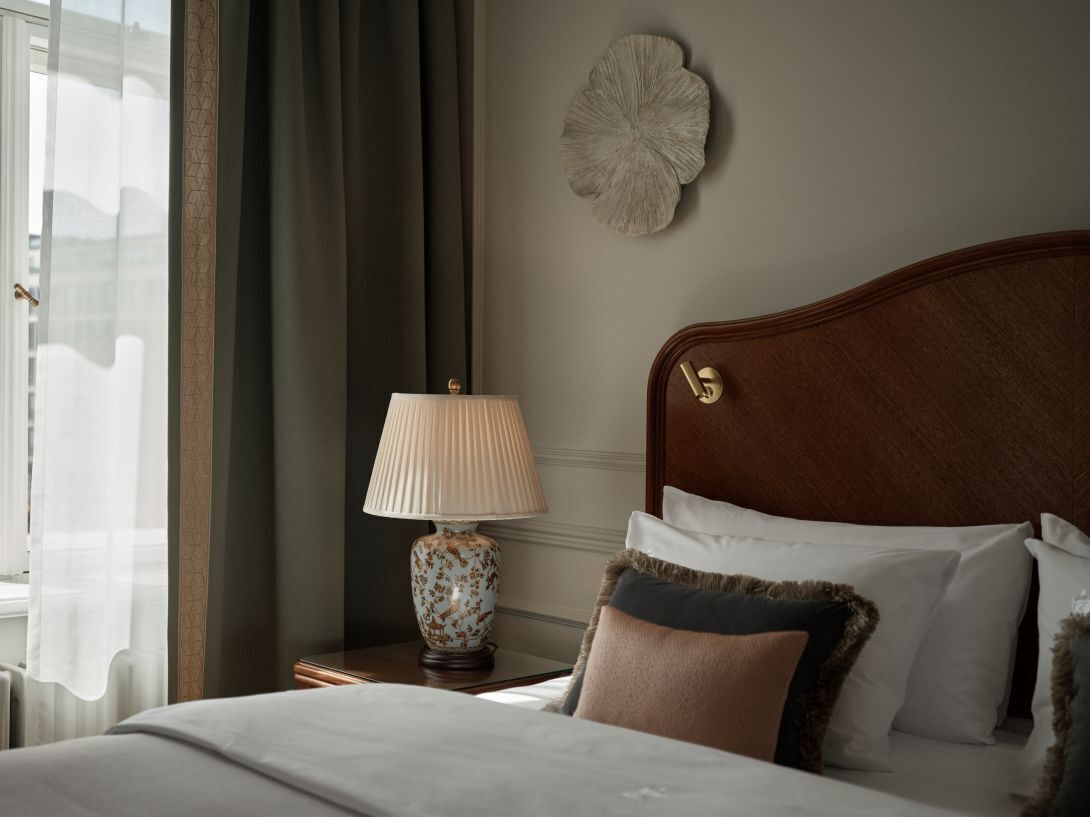 Una cama bien tendida con un cabecero de madera, una lámpara de noche y almohadas decorativas.