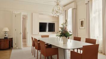 A spacious dining area with a large table, chairs, a chandelier, and a television mounted on the wall.