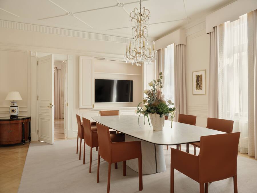 A spacious dining area with a large table, chairs, a chandelier, and a television mounted on the wall.