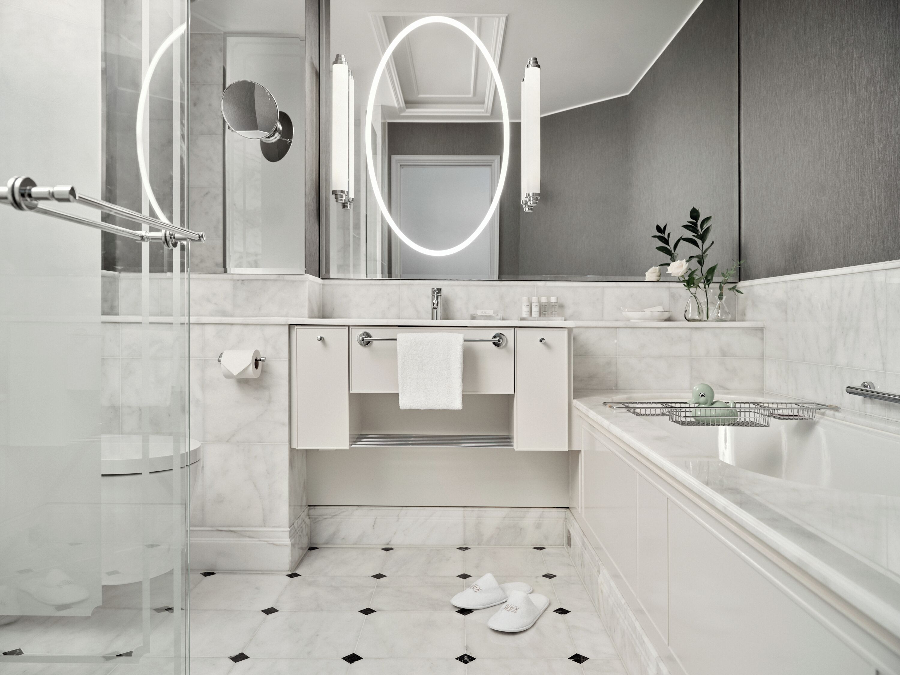 Un baño moderno con mampara de vidrio, tocador blanco con perchero y bañera con asiento para ducha.