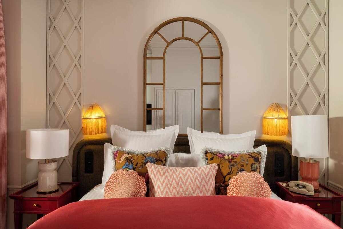 A neatly arranged bedroom with a large mirror, two bedside tables with lamps, and a variety of pillows.
