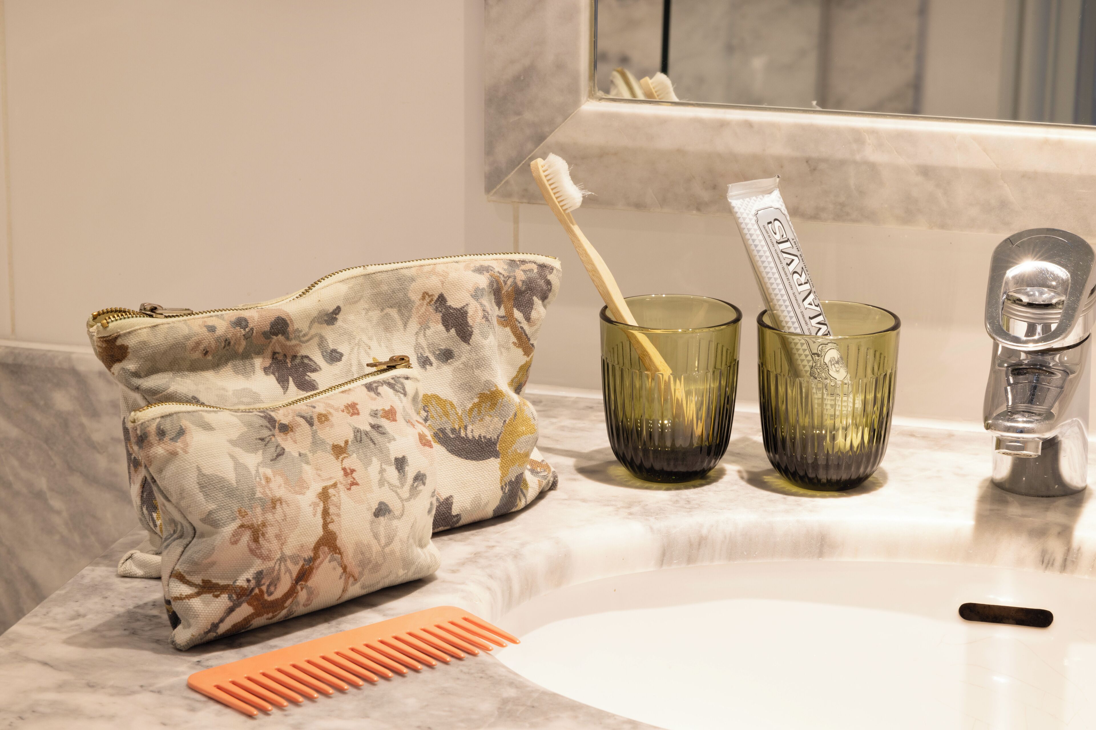 Un lavamanos con espejo, un bolso estampado con motivos florales, dos cepillos de dientes y un peine.