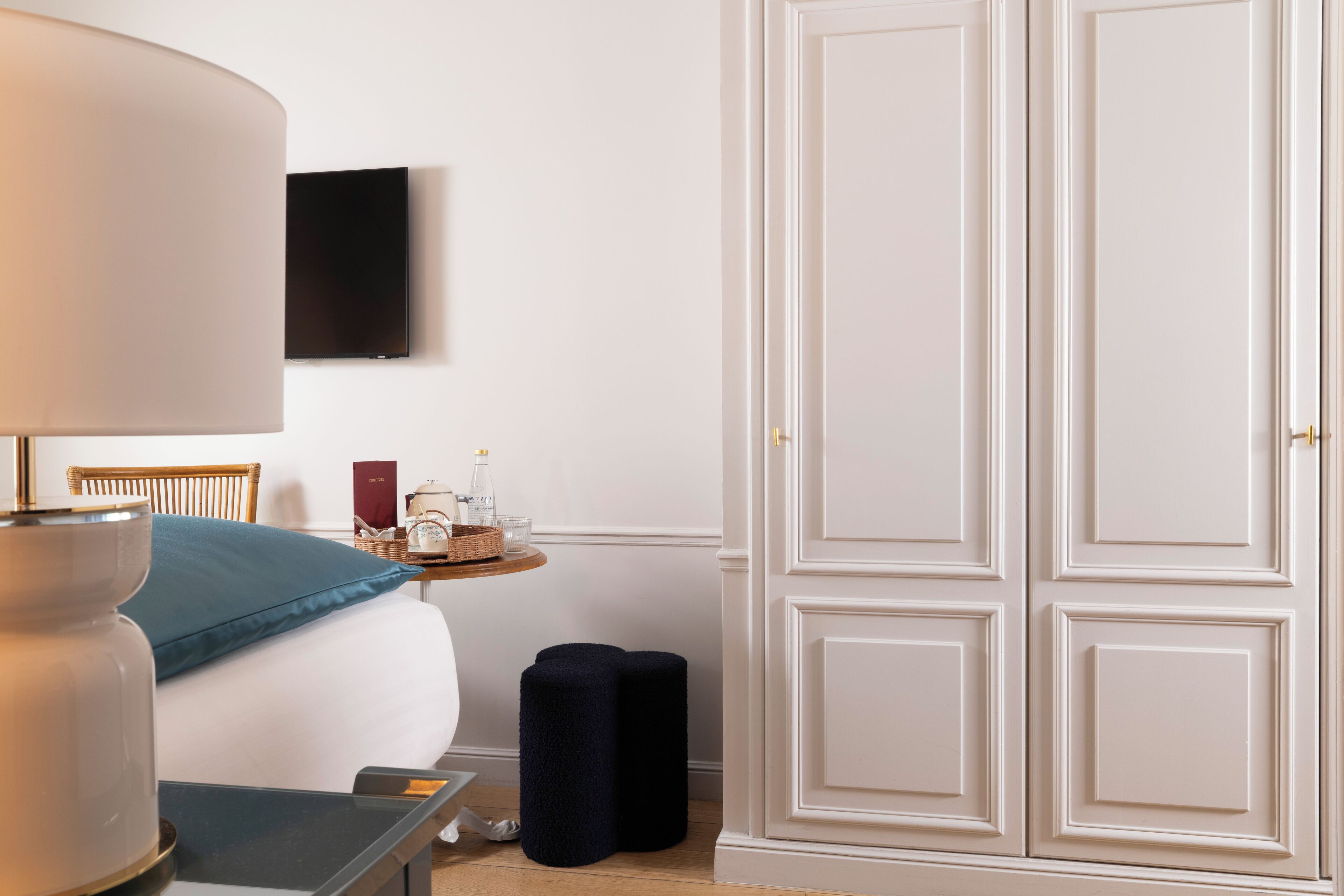 A hotel room with a bed, a bedside table with a lamp, a TV mounted on the wall, and a wardrobe.