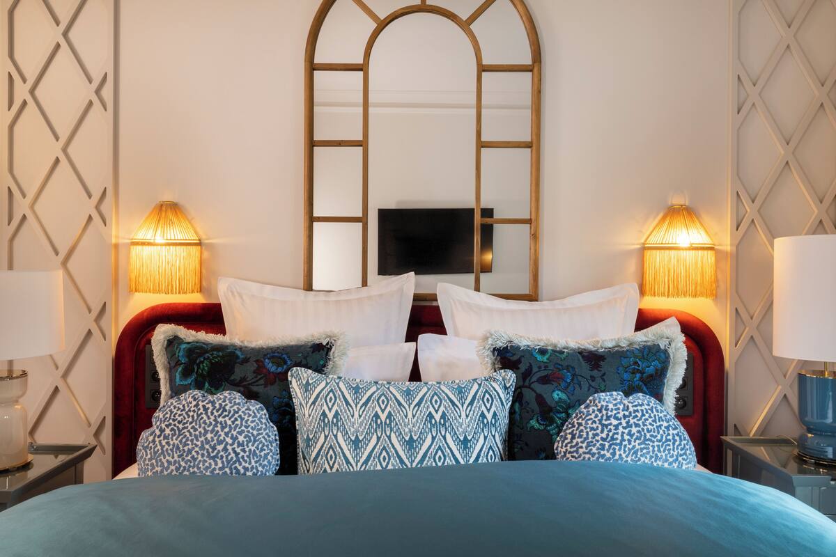 A neatly made bed with patterned pillows, a red headboard, and two bedside lamps.