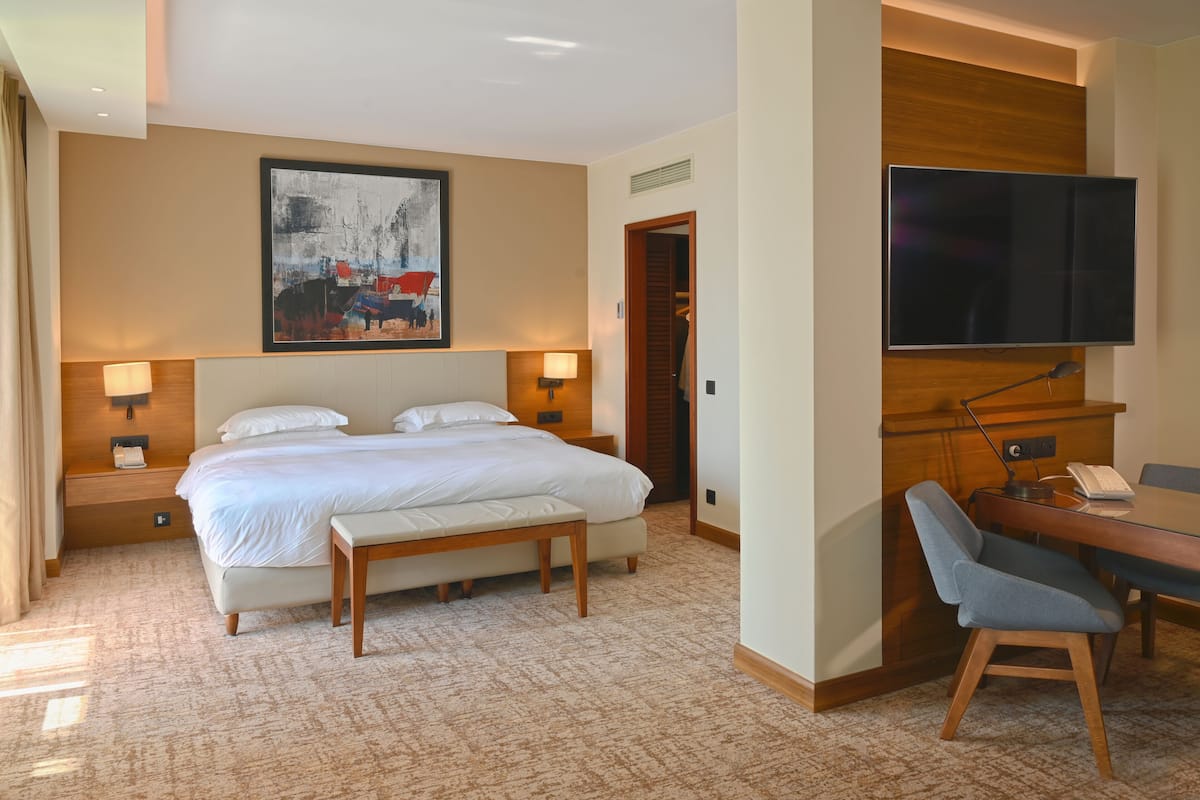 A hotel room with a large bed, bedside lamps, a desk with a chair, a flat-screen TV, and a painting on the wall.