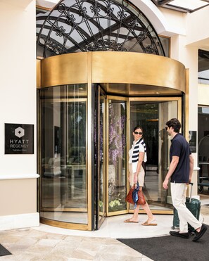 Entrada giratoria a un hotel con puerta de vidrio, un cartel que dice 'HYATT REGENCY' y un techo metálico decorativo.