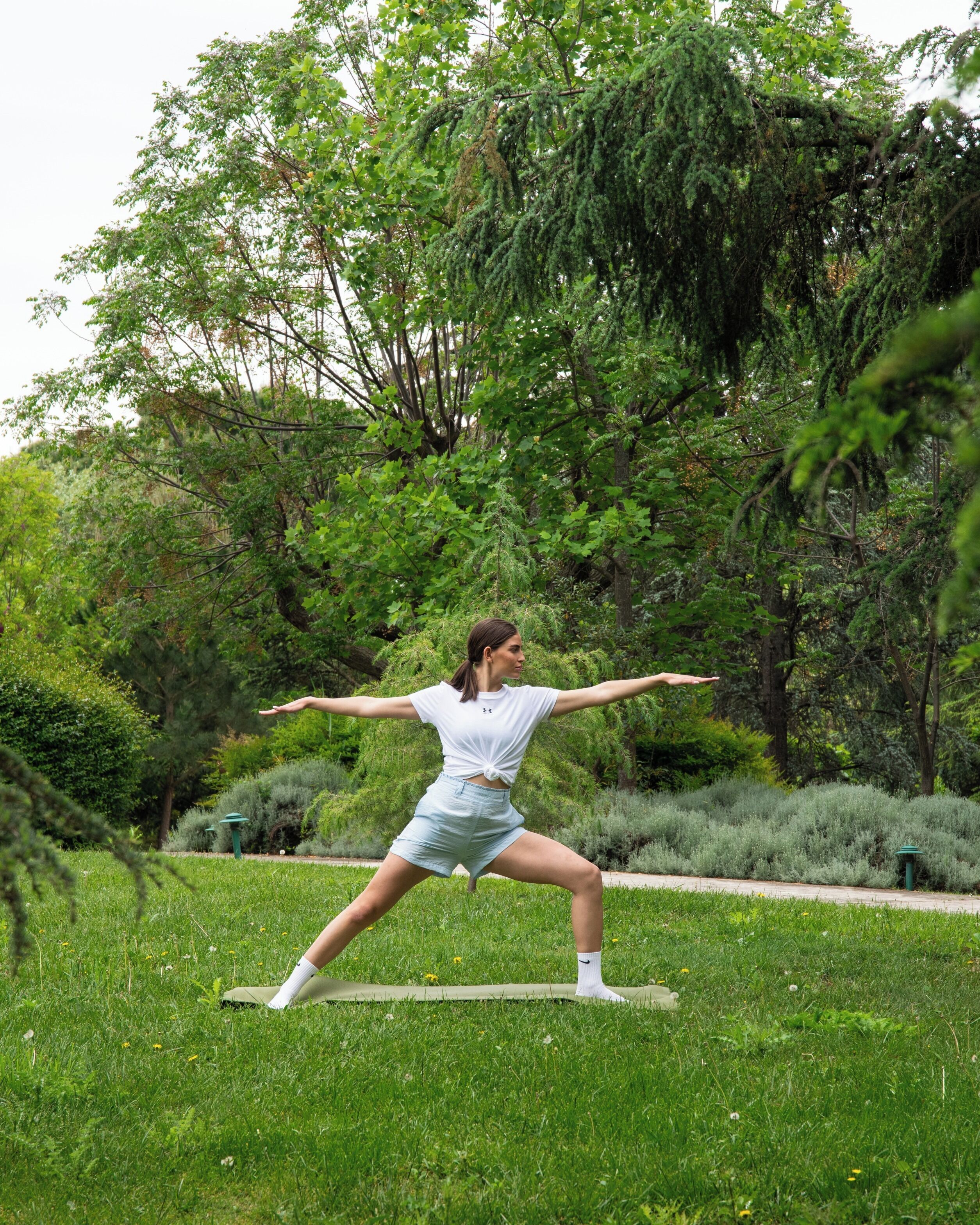A person performing a yoga pose in a park with lush greenery and trees in the background.