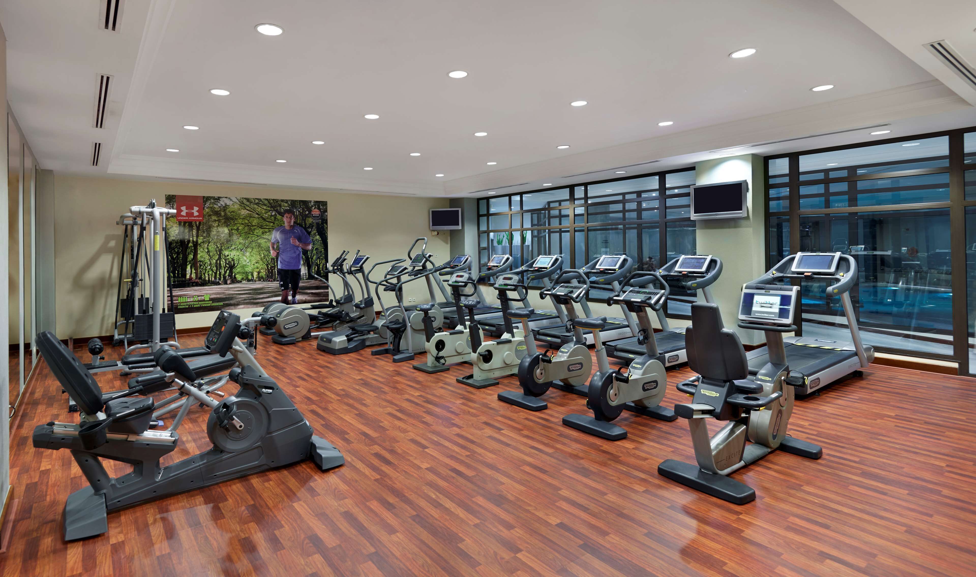 Ett gym med flera löpband, crosstrainers och styrketräningsmaskiner, stora fönster och ett trägolv.
