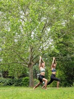 Two people performing yoga in a grassy area with trees in the background.