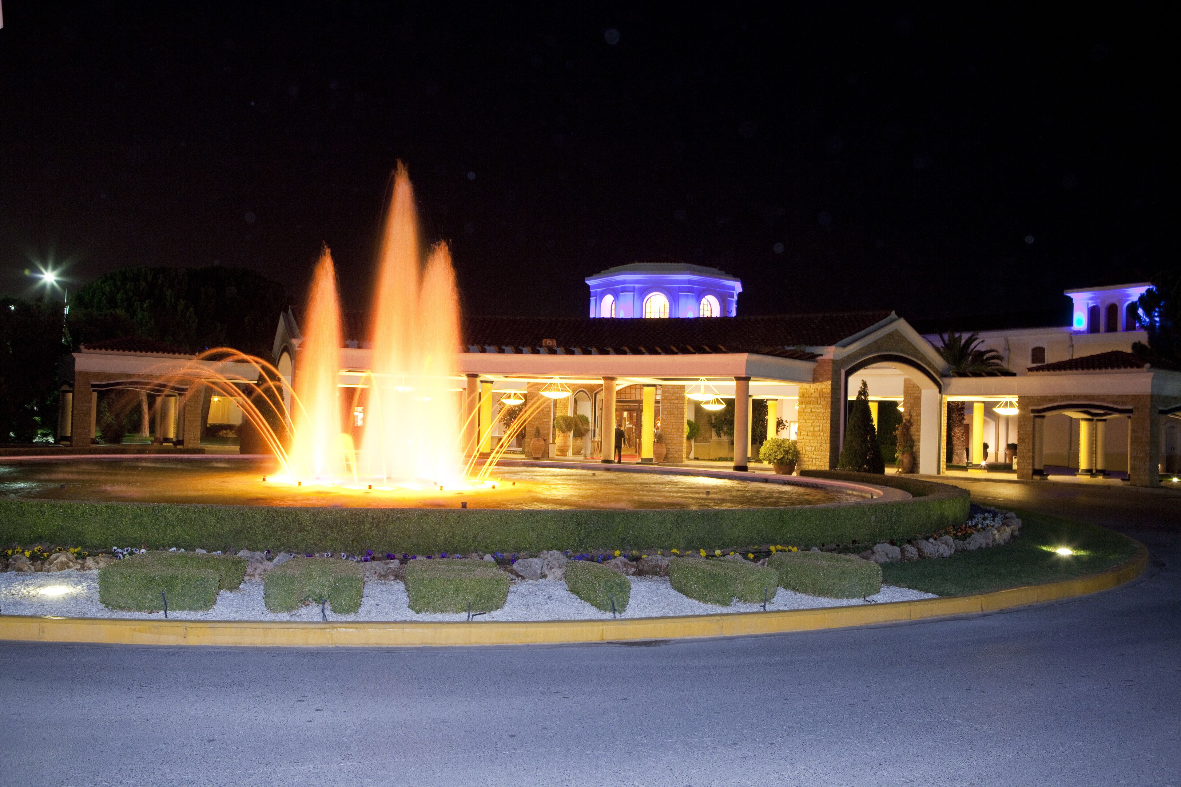 A hotel with a fountain in front, a landscaped garden, and a building with a dome and arches.