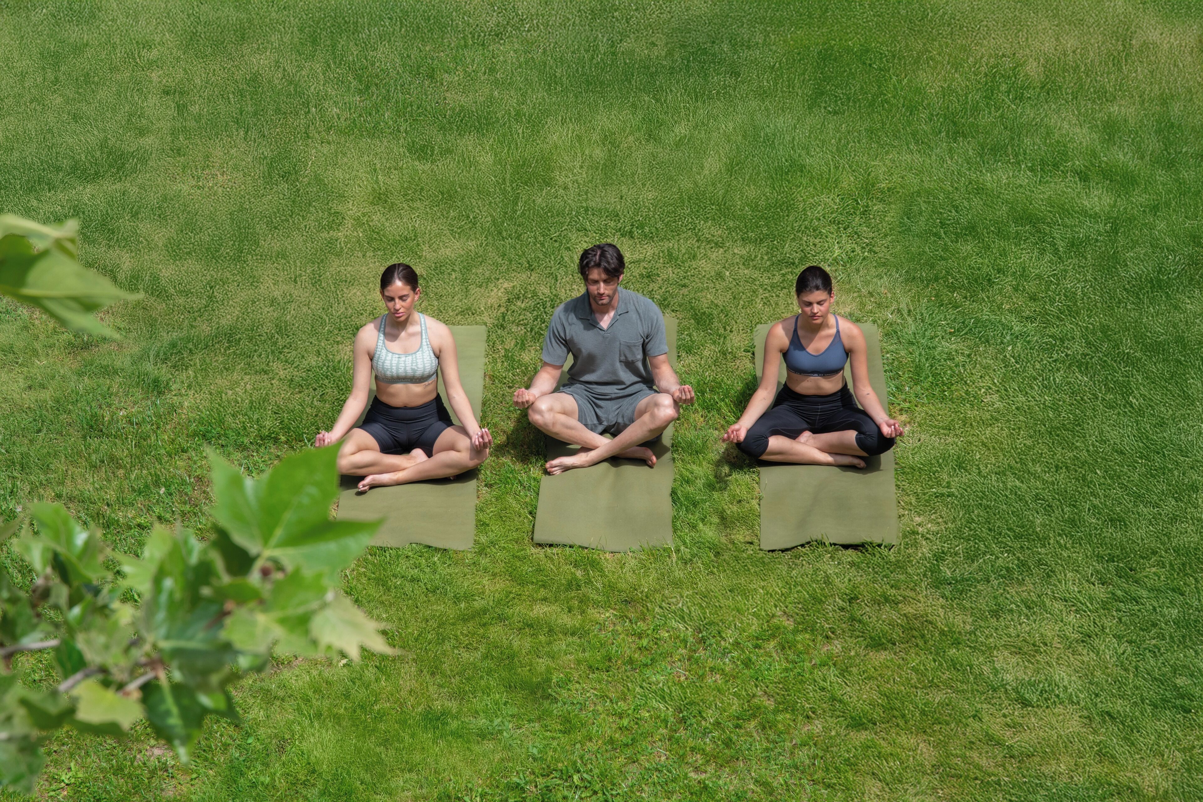 Three individuals sitting on mats in a grassy outdoor area.