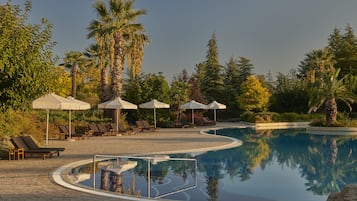 Un espace piscine agrémenté de chaises longues et de parasols, entouré de palmiers et de verdure.
