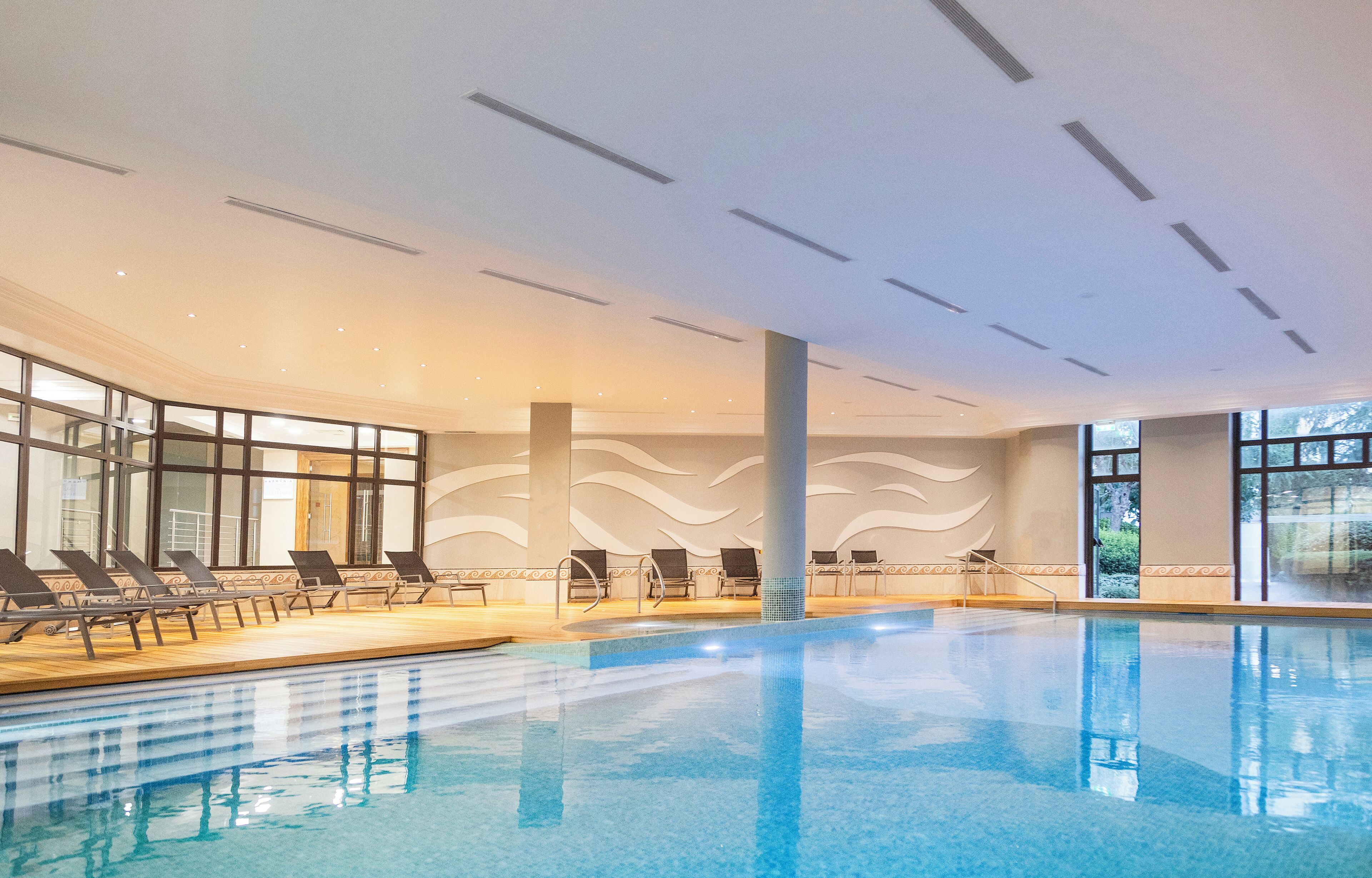 An indoor swimming pool with lounge chairs and large windows.
